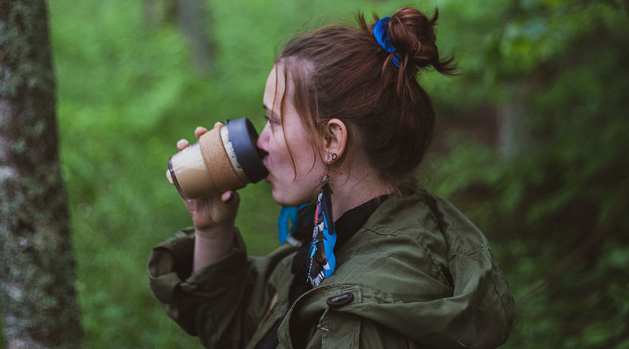 woman drinking from a reusable cup in forest