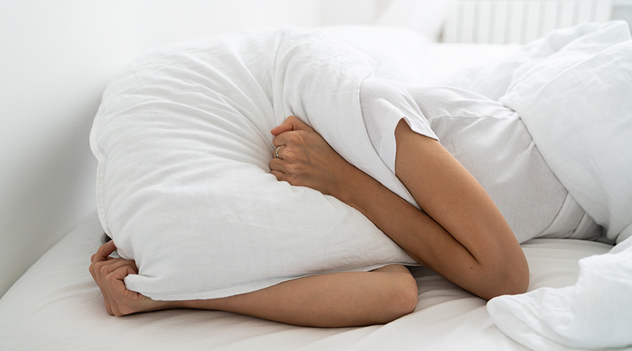 woman in bed holding pillow over her head to block out a noisy neighbor or roommate